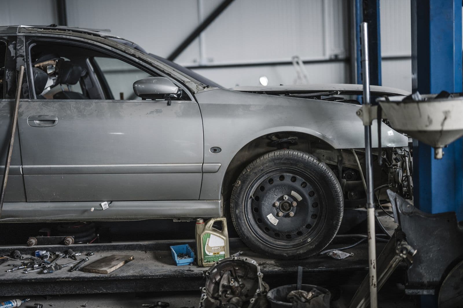 A grey sedan with its front wheel off, up on a lift in a repair shop