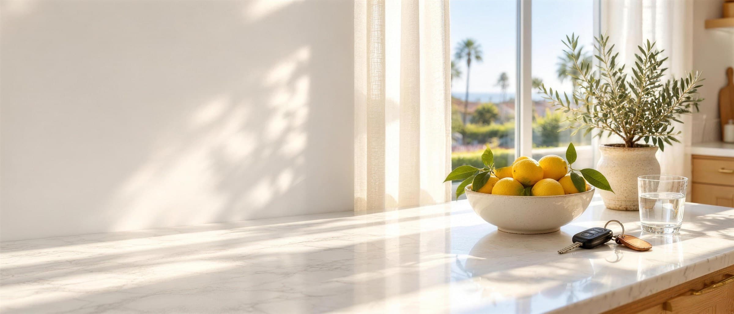 Sunlit kitchen counter with a bowl of lemons, car keys and a glass of water